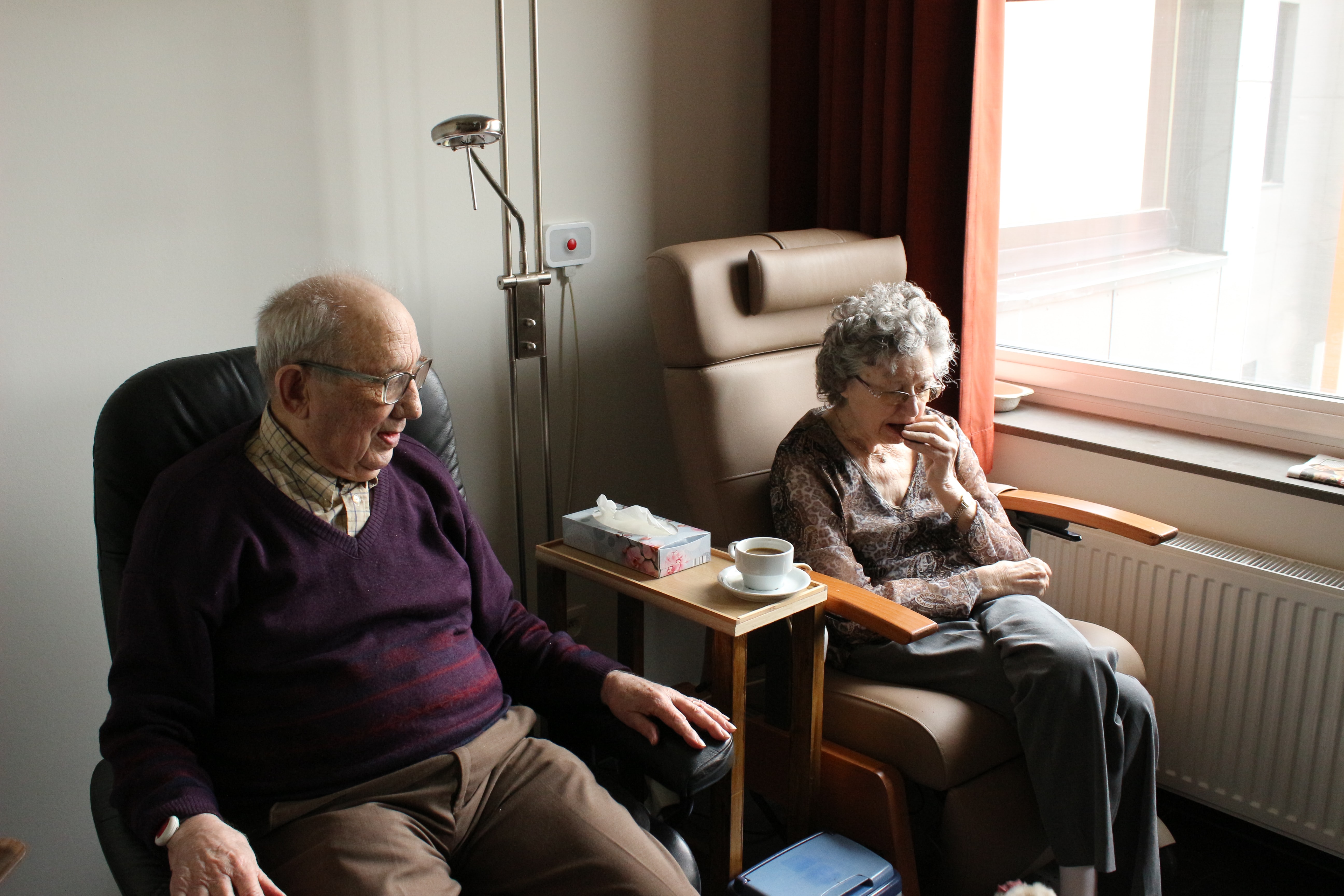 Una parella de persones d'edat avançada asseguts en una cambra d'un centre residencial.